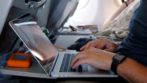 Close-up-male-hands-with-smart-watch-using-laptop-to-work-online-during-comfortable-airplane-business-trip-flight.