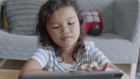 Asiatische-kleine-Mädchen-mit-Tablet-digital,-spielen,-während-im-Wohnzimmer-zu-Hause-sitzen