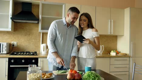 Atractiva-pareja-se-reúnen-en-la-cocina-temprano-en-la-mañana.-Hermosa-mujer-usando-tableta-compartir-las-redes-sociales-de-su-marido