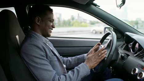 Smiling-mixed-race-businessman-surfing-social-media-on-his-tablet-computer-sitting-inside-his-car