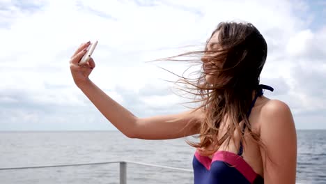 girl-with-braces-on-her-teeth,-young-female-in-swimsuit-Photographed-on-mobile-to-waterfront-ocean,-Selfi-of-girl-in-bathing-suit-on-coast-sea