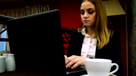 Businesswoman-typing-text-on-a-laptop-sitting-in-a-cafe-over-a-Cup-of-tea