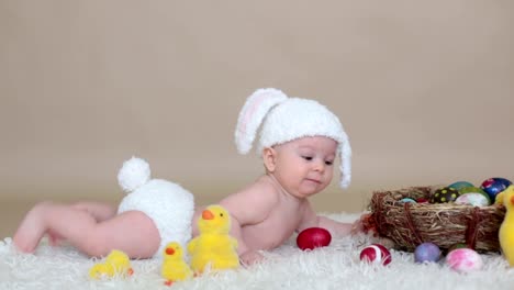 Cute-little-toddler-baby-boy,-playing-with-colorful-easter-eggs-and-little-decorative-ducks,-isolated-shot,-beige-background