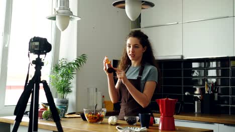 Attractive-girl-recording-video-food-vlog-about-healthy-cooking-on-digital-camera-in-the-kitchen-at-home.-Vlogging-and-social-media-concept