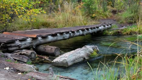 Paseo-marítimo-de-madera-pequeño-puente-sobre-Arroyo-de-bosque-cerca-del-lago-azul-Geyser-en-montañas-de-Altai-en-día-de-lluvia