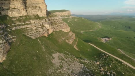 Antenne:-Flug-über-eine-hohe-Felswand,-offenbart-einen-Blick-des-Passes-in-Russland-im-Nordkaukasus.-Luftaufnahmen-von-der-Straße-in-der-untergehenden-Sonne.-Flug-neben-dem-Felsen