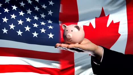 US-investment-in-Canada,-hand-putting-money-in-piggybank-on-flag-background