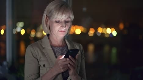 Mid-Aged-Businesswoman-Typing-on-Smartphone-in-Dark-Office