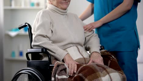 Enfermera-cubriendo-suavemente-con-mujer-de-manta-en-silla-de-ruedas,-cuidado-de-ancianos