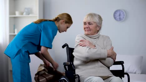 Nette-Krankenschwester-mit-Decke-für-Behinderte-alte-Frau,-die-vor-Kälte-zitternd