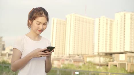 Fröhliche-asiatische-Touristenbloggerin-mit-Touchscreen-Technologie-auf-dem-Smartphone,-während-zu-Fuß-auf-der-Straße-in-der-Innenstadt-am-Abend.-Lifestyle-Rucksack-Touristie-Reise-Urlaubskonzept.