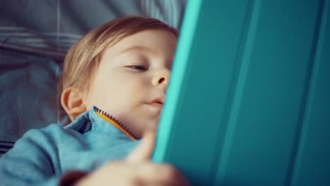 Un-niño-mirando-su-tableta-en-la-cama-en-casa