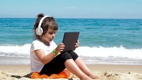 Niño-usando-tableta-en-la-playa.-Niño-usando-auriculares.