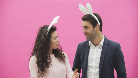 Young-couple-standing-standing-on-pink-background.-During-this-time,-they-are-dressed-in-rabble-ears.-Looking-at-each-other,-talk-and-smile.