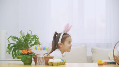 Joyful-playing-girl-with-bunny-ears-on-his-head-is-hiding-under-the-wooden-table-by-a-slow-pace.-Girl-is-dowing-down-slowly-hiding-herself.