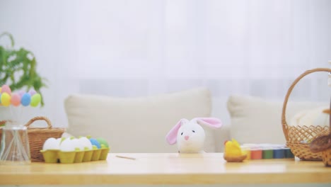 Joven-chica-adorable-se-esconde-bajo-la-mesa-llena-de-decoraciones-de-Pascua-y-está-jugando-con-el-conejo-de-Pascua-en-la-mano.-Bunny-invita-a-la-chica-a-se-un-mundo-maravilloso.