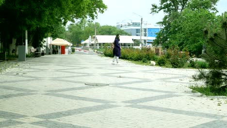 La-mujer-camina-a-lo-largo-del-callejón-entre-los-árboles-en-la-acera.