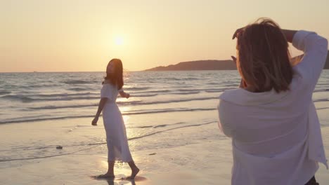 Young-Asian-lesbian-couple-using-camera-taking-photo-each-other-near-beach.-Beautiful-women-lgbt-couple-happy-romantic-moment-when-sunset-in-evening.-Lifestyle-lesbian-couple-travel-on-beach-concept.