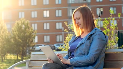 Frau-mit-Tablet-Computer-sitzt-auf-Bank-in-der-Stadt