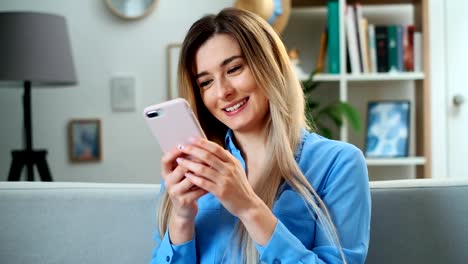 Retrato-de-la-chica-usando-el-dispositivo-móvil-navegando-por-Internet,-manteniéndose-conectado-en-casa-disfrutando-de-un-estilo-de-vida-moderno.-Mujer-bastante-joven-usando-el-teléfono-inteligente-en-el-sofá,-enviando-mensajes-de-texto-mientras-se-rel