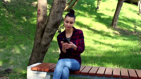 Young-beautiful-girl-in-a-plaid-shirt-smiling-and-browsing-the-tape-of-social-networks-in-her-smartphone.