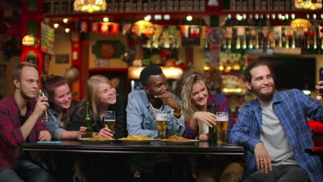 In-der-Bar-oder-im-Restaurant-nimmt-hispanic-man-Selfie-von-sich-und-ihren-besten-Freunden.-Gruppe-Schöne-junge-Menschen-in-stilvollen-Establishment