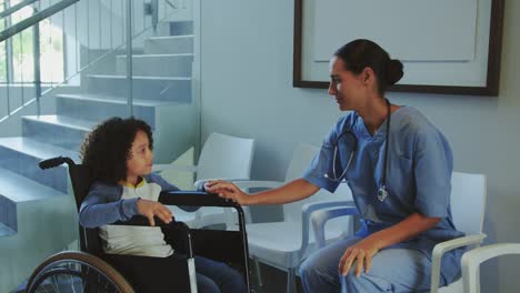 Vista-frontal-de-la-doctora-caucásica-interactuando-con-un-niño-discapacitado-en-el-pasillo-del-hospital-4k