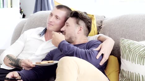 Gay-couple-relaxing-on-couch.-Watching-tv-and-enjoy-cookies.