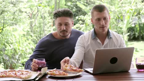 Gay-couple-having-pizza-for-lunch.-Typing-on-laptop.