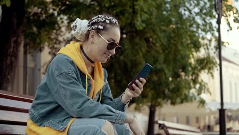 Woman-texting-with-mobile-phone,-typing-text-message-sitting-at-bench