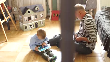 Grandpa-looks-photo-album-with-his-wedding,-little-boy-using-electronic-tablet