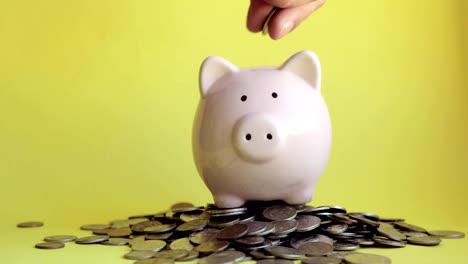 Man-putting-coins-in-piggy-bank-standing-in-pile-of-coins,-hand-closeup