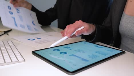 Business-man-and-woman-working-on-tablet-computer-and-analyzing-a-marketing-report-on-white-desk