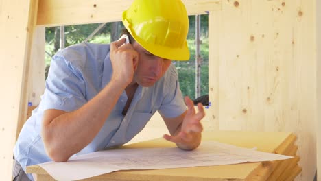 CLOSE-UP:-Mann-streitet-am-Telefon-mit-Architekt,-während-er-sich-Blaupausen-ansieht