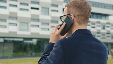 Der-Geschäftsmann-telefoniert.-Er-trägt-Anzug-und-Brille.-Das-Business-Center-befindet-sich-im-Hintergrund.-Nahaufnahmen.-4K