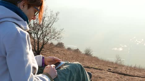 Mujer-con-el-teléfono-inteligente-al-aire-libre.-Partes-del-cuerpo-en-contraluz,-vista-lateral-trasera.