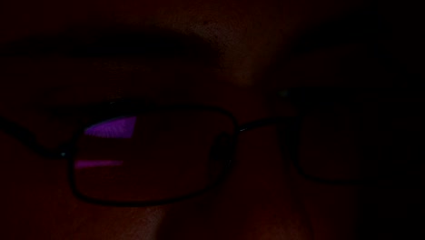 Closeup-of-teenager-eyes-wearing-glasses-and-browsing-internet-on-tablet-pc-in-a-dark-room