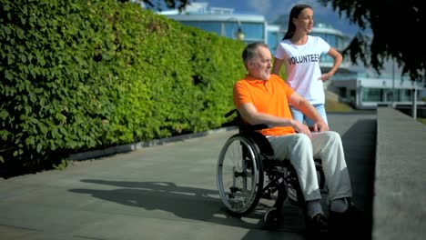 Helpful-female-volunteer-resting-with-a-wheelchaired-man