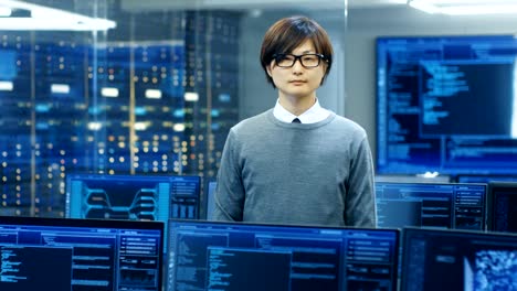 In-the-System-Control-Room-Technical-Operator-Stands-and-Looks-at-the-Camera.-He's-Surrounded-by-Multiple-Displays-Showing-Graphics.-IT-Technician-Works-on-Artificial-Intelligence,-Big-Data-Mining,-Neural-Network-Project.