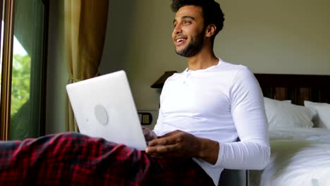 Young-Hispanic-Man-Using-Laptop-Computer-Happy-Smiling-Guy-Chatting-Online-Over-Big-Window-With-Tropical-Garden-View