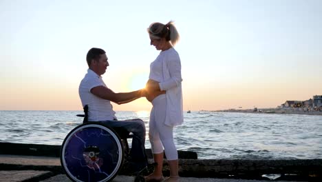 handicapped-person-in-wheelchair-listens-belly-of-his-wife-on-background-sea