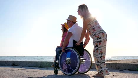 parents-with-child-on-rest,-happy-pregnant-woman-with-little-girl-and-handicapped-person-in-backlight-daughter-sits-on-disabled-daddy