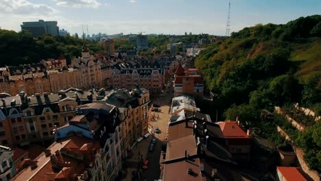 Zángano-de-la-cámara-se-mueve-bajo-techos-de-edificios-en-antigua-europeas-callejuelas-con-casas-de-colores-y-los-peatones-al-atardecer-4K