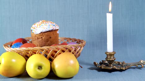 Reise-Kameras,-Ostern-Arrangement,-Ostern-in-den-hölzernen-Korb-mit-bemalten-Eiern-und-Apfel,-in-der-Nähe-von-die-weiße-Kerze-in-der-Bronze-Leuchter