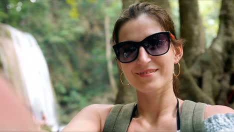 Happy-woman-tourist-on-vacation-posing-in-front-of-waterfalls-in-tropical-park