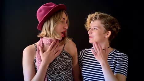 Two-young-blonde-pretty-women-standing-close-and-talking,-happy-and-cheerful,-isolated-on-black-background