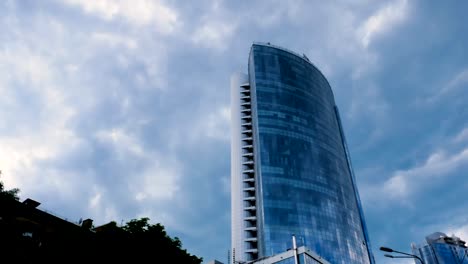 Vídeo-de-lapso-de-tiempo.-Una-vista-desde-abajo-en-un-centro-de-negocios-de-vidrio-sobre-un-fondo-de-nubes-grises-en-movimiento