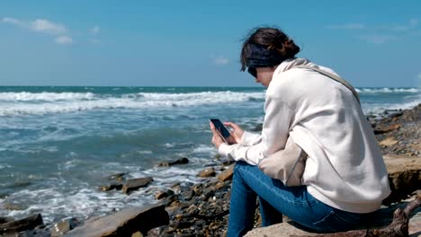 Frau-spielt-das-Spiel-am-Telefon-sitzen-am-Ufer-Meeres-im-Herbst.