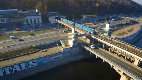 Antenne,-Top-Aussicht-von-Drone:-Metro-Zug-fährt-über-eine-Brücke-mit-PKW-und-LKW.