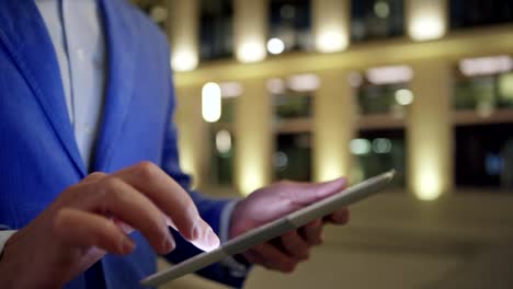 Hands-of-businessman-using-tablet-computer-in-night-street,-close-up-of-man-tapping-and-swiping-touchscreen-while-browsing-Internet-outdoors